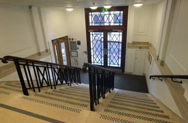 A wide flight of 11 steps with four handrails. At the foot of the stairs is large doorway leading out onto a road.