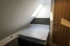 A single bed with a sloped ceiling and skylight over it.