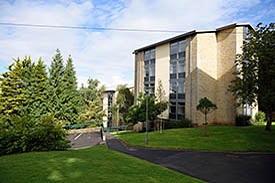 Two five-storey modern residential blocks, with trees and green space in the foreground.