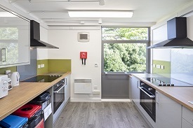A kitchen with two ovens and hobs, a fire blanket, recycling bins and several cupboards.