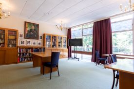 A room with bookcases, several desks and chairs, and a television on a stand.