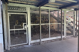 A bike storage space with two levels of bike rack. The storage is behind a metal fence with two locked gates.