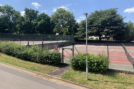 Two pairs of tennis courts at the side of a sloped road.