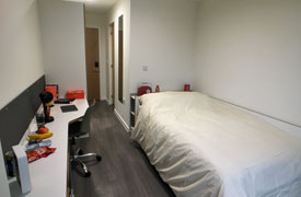 A room with a double bed in one corner and a desk with an office chair against the opposite wall.