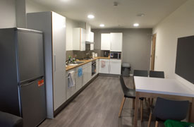 A kitchen with a fridge freezer, a sink, an oven and hob, and several cupboards and drawers. There is a dining table opposite with four chairs around it.