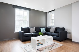 A room with a large black leather corner sofa around a coffee table.