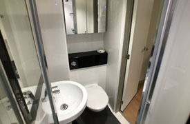 A bathroom with a toilet, sink, shower and medicine cabinet with mirrored doors.