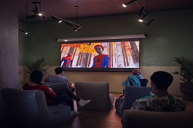 Four people of different races and genders sitting on armchairs and watching 'Spider-Man: Into the Spider-Verse' on a screen on the wall.