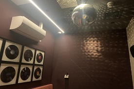 A karaoke room with a glitter ball on the ceiling. To the left there are some records stuck on the wall and in the right of the image is the karaoke screen.
