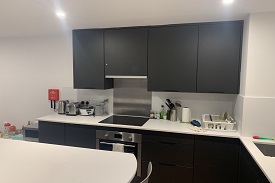 Kitchen surfaces with appliances on them and kitchen cupboards above with the kitchen table in the bottom of the image.