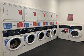 A series of six washing macchines and six tumble dryers on top of eachother in a room.