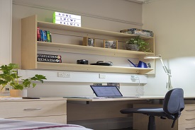 A desk with an office chair beside it, drawers beneath it and shelves above it.