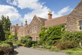 Exterior of a large three-storey red brick redidential building, with a garden in front of it.