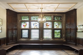 A room with wooden benches and panels and stained glass windows.