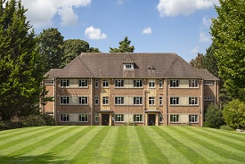 Exterior of a large four-storey red brick redidential building, with a lawn in front of it.