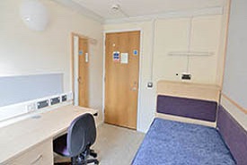 A room with a single bed against one wall and a desk and office chair opposite.