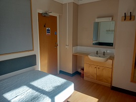 A room with a single bed in one corner and a basin with a cupboard beneath and a mirror above.