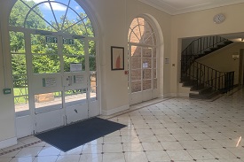 A hallway with two large doors leading to a veranda and garden outside. There is a stairwell indoors leading both upstairs and downstairs.