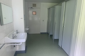 A room with four toilet stalls, two sinks and a mirror.