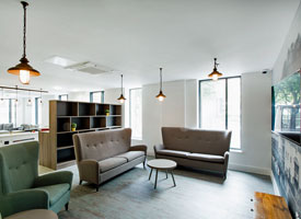 Communal area with two sofas, armchair, small tables, wall-mounted television, shelves and in the background a pool table and more sofa seating