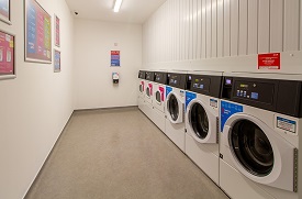 A laundry room with a row of six washing machines and tumble dryers against one wall.
