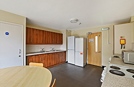 A kitchen with a dining table and two chairs, two sinks, two ovens and hobs, two fridge freezers and lots of cupboards.