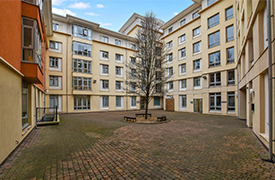 A paved courtyard enclosed on four sides by a seven-storey building, with a tree in the centre.
