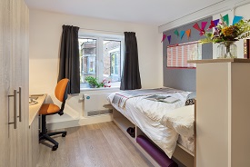 A room with a double bed in one corner and a desk, office chair and cupboard opposite.