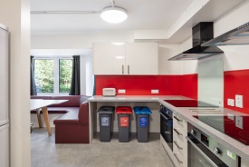 A kitchen with two ovens and hobs, three recycling bins, and a booth of seats around a table.