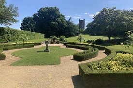 A garden with hedges and flowerbeds shaped around the path, and a tower in the distance.