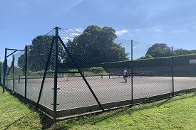 A row of four tennis courts behind a tall fence.
