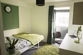 A room with a double bed against one wall and a desk with a chair opposite.