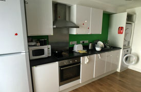 A kitchen with an oven and hob, a fridge freezer, washing machine, tumble dryer, and several cupboards.