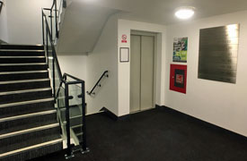 A landing with a stairwell leading up and down and a lift next to it. The sign on the wall shows that there are six storeys.
