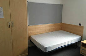 A double bed in the corner of the room, with a wardrobe at the foot of the bed.
