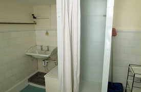 A bathroom with a sink and a shower cubicle. There is a mop and bucket to the side of the cubicle.