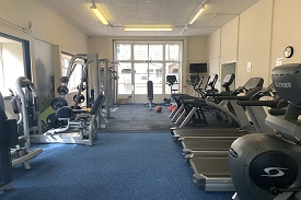 A room containing exercise equipment, including treadmills, crossfit machines, exercise bikes, and weight machines.