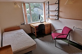 A single bed to the left of the room with a desk and chair in the far right corner of the room next to the window.