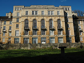 The exterior of a large six-storey sandstone building with a garden lawn in front of it.
