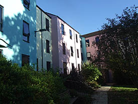 A grassy courtyard surrounded by three-storey buildings of different colours. There is a path with steps leading up to the buildings.