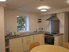 A kitchen with an oven and hob, a sink, a dining table with three chairs around it, and lots of cupboards and drawers.