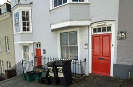 Exterior of row of terraced three-storey houses with the numbers 43 and 45 on the walls by the doors. There are recycling bins outside and a set of steps on the pavement.