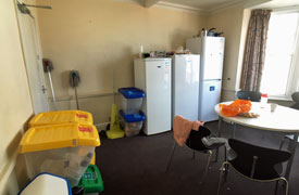 A room with several fridge freezers, a table surrounded by four chairs, and several clear plastic storage boxes.