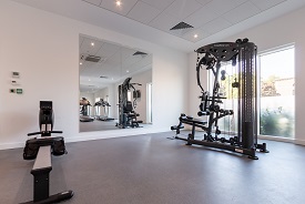 A room with a rowing machine, a weight machine, and large mirrors on the wall opposite them.