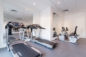 A room with two treadmills, two exercise bikes, and tall mirrors on the walls in front of them.