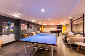 A large room with several sofas and armchairs, a pool table and a ping pong table.