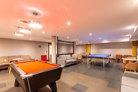 A large room with several sofas, two tables with chairs around them, a pool table and a ping pong table.