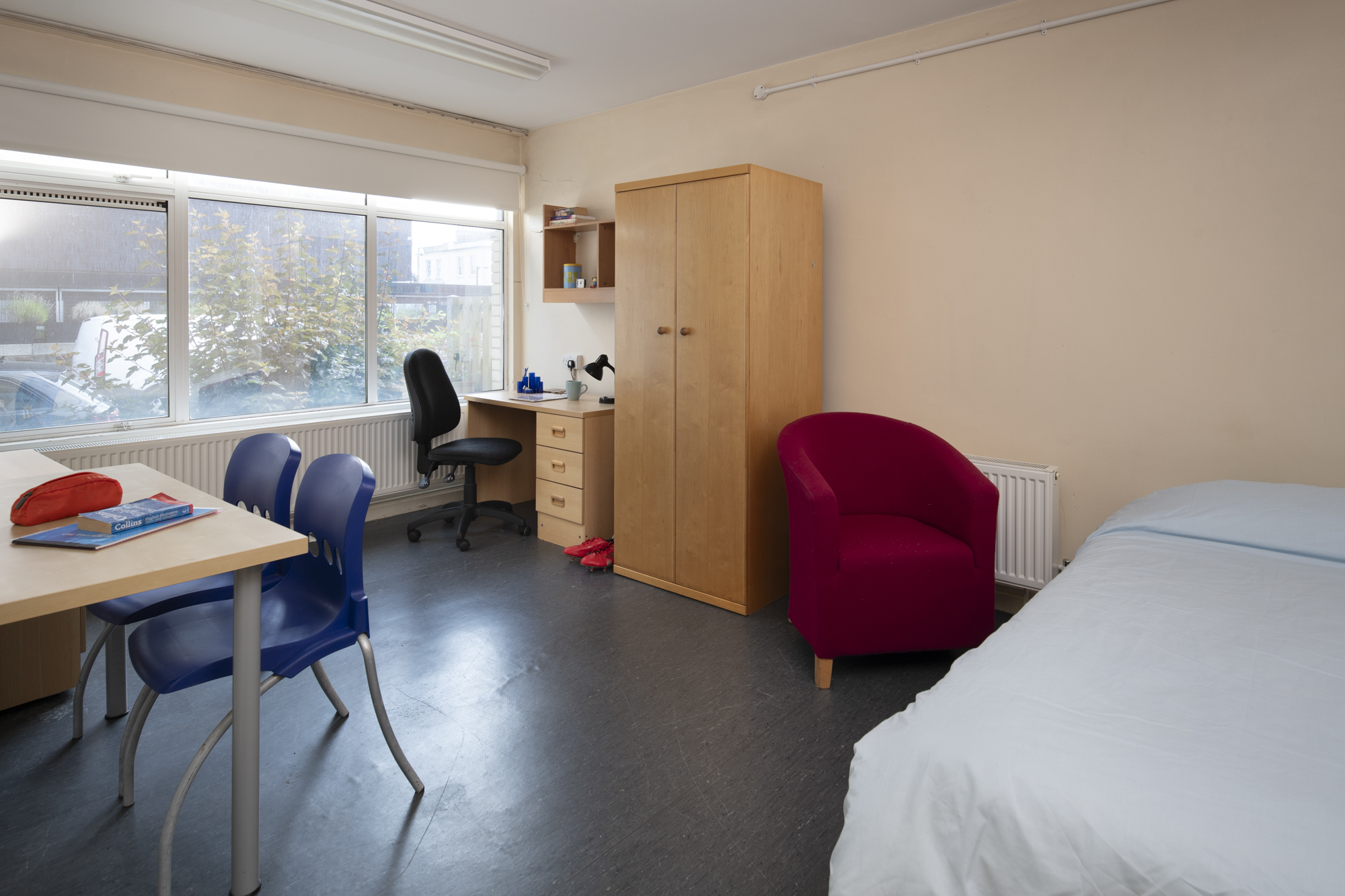 View of bedroom showing single bed, desks and chairs, armchair, storage units, shelves, radiator, and large windows