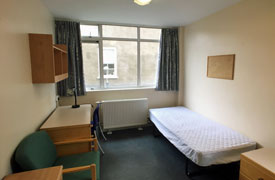 View of bedroom showing single bed, desk and chair, armchair, storage units, shelves and radiator