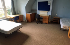 A bedroom with two double beds and 2 desks. There is one office chair and one side chair.